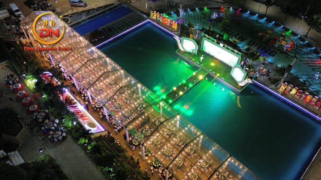 Ảnh flycam một nhà bạt truss nhôm khổng lồ trong một lễ hội âm nhạc buổi tối, đèn sáng rực rỡ.